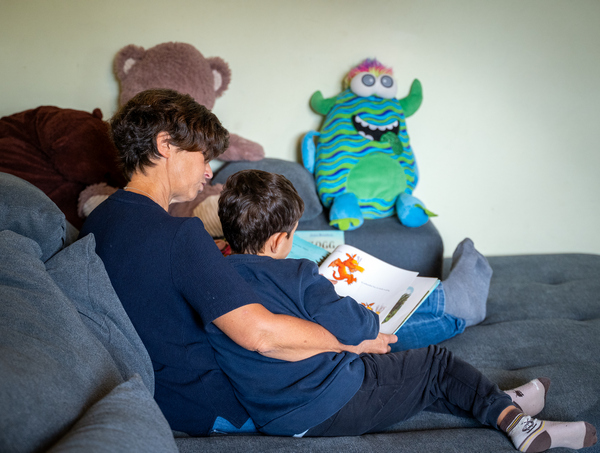 Eine Erzieherin sitzt mit einem Jungen auf dem Sofa und liest aus einem Buch vor.