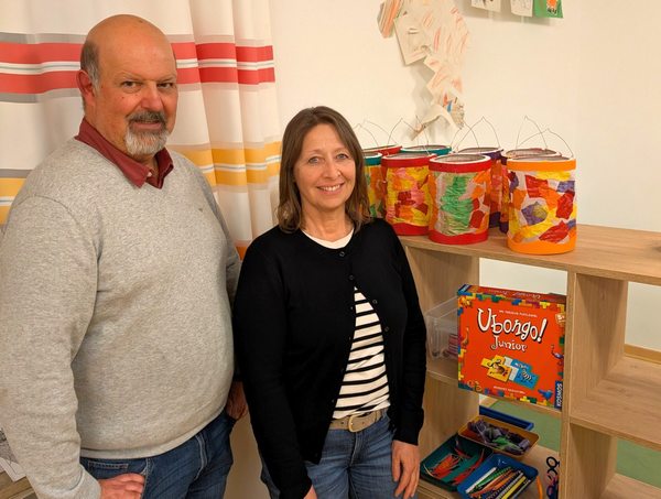 Hausleiter und Gruppenleiterin vor Regal mit Kinderspielen