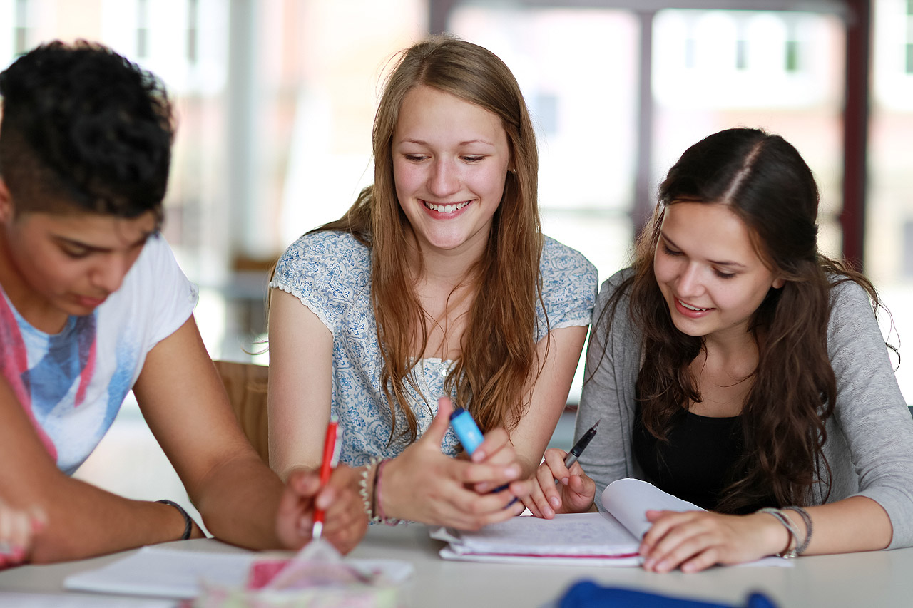 Drei Studenten sprechen über ihre Studienarbeiten an einem Tisch.
