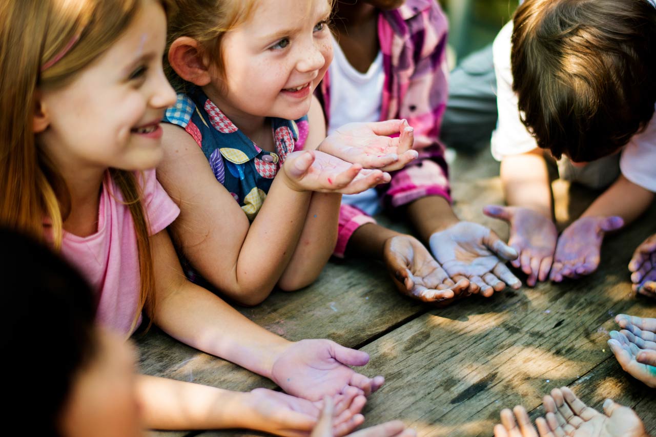 Kinder rund um einen Tisch, die die Hände nach oben offen halten.