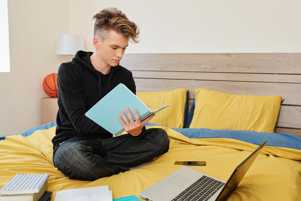 Ein junge sitzt auf einem Bett und liest ein Buch.