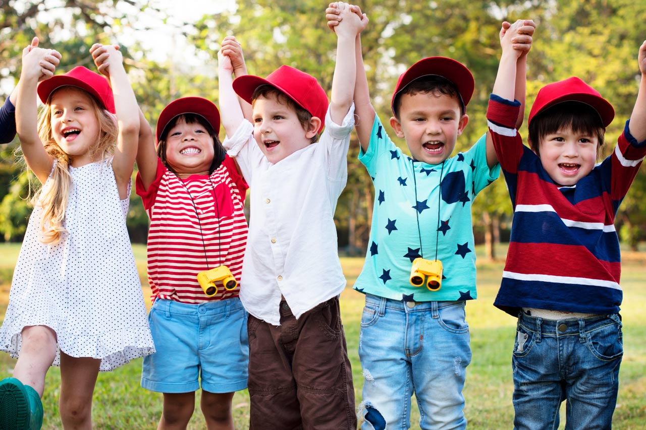 Eine Gruppe Kinder reckt die Hände in die Höhe auf einer Wiese.